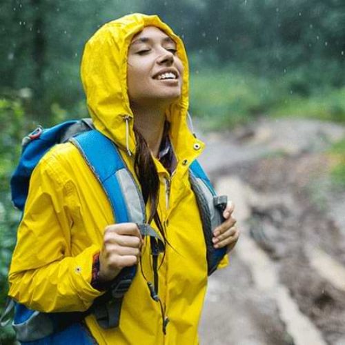 Woman in a yellow raincoat smiling while hiking in the rain in Arenal, Costa Rica.