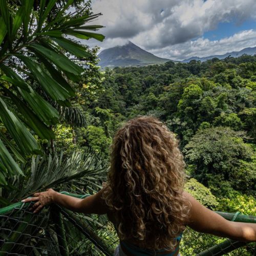 Woman with curly hair enjoying the peaceful view of Arenal Volcano and lush green forest at Wellness Park.